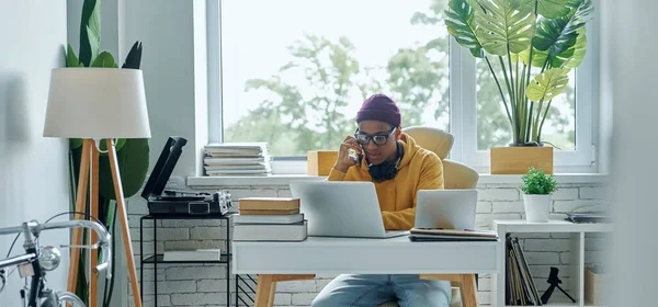 Genç melez ırk adamı ofiste çalışırken cep telefonuyla konuşuyor.