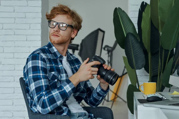 Sebevědomý Mladý Muž Drží Digitální Fotoaparát Zatímco Sedí Svém Pracovišti — Stock fotografie