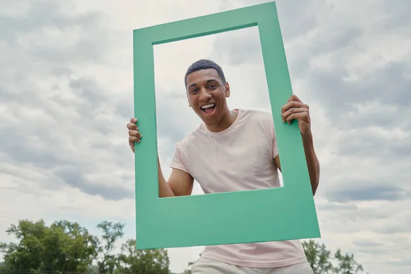 Happy Mixed Race Man Looking Picture Frame While Standing Outdoors — Stock Photo, Image