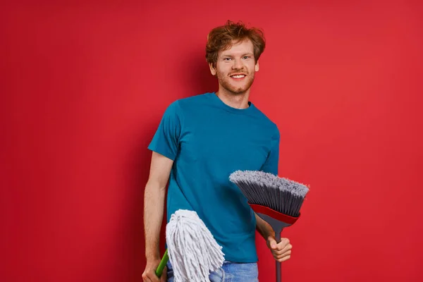 Χαρούμενος Νεαρός Που Κουβαλάει Εξοπλισμό Καθαρισμού Ενώ Βρίσκεται Κόκκινο Φόντο — Φωτογραφία Αρχείου