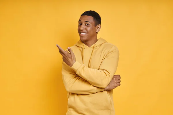 Cheerful mixed race man pointing away while standing against yellow background