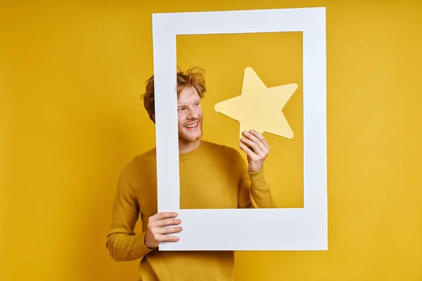 Szczęśliwy Człowiek Trzyma Gwiazdę Patrząc Przez Ramkę Obraz Żółtym Tle — Zdjęcie stockowe