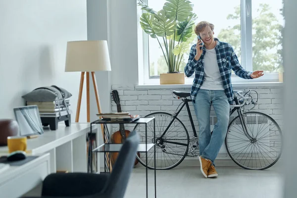 快乐的年轻人站在客厅的自行车旁边 手里拿着手机 — 图库照片