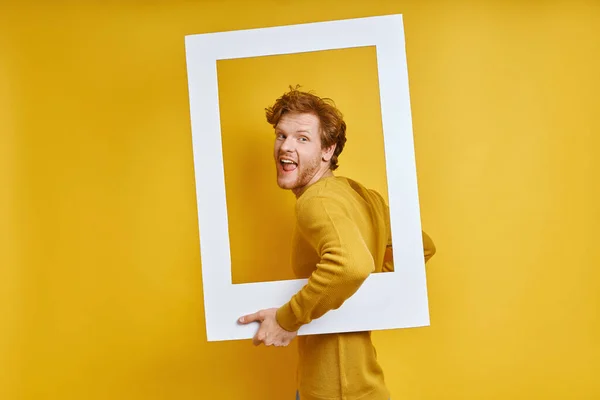 陽気な赤毛男を見ながら画像フレームを通して黄色の背景 — ストック写真