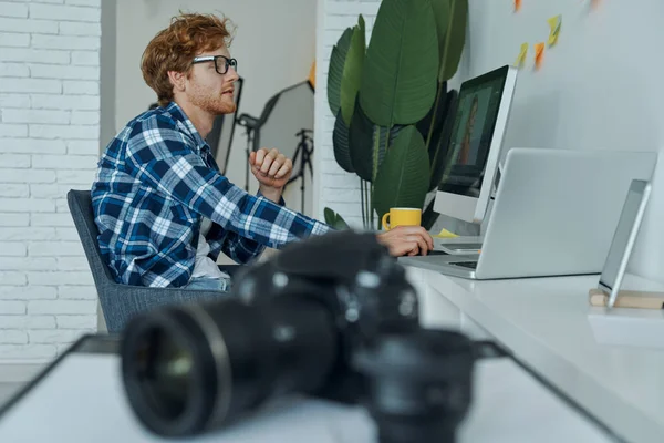 Důvěryhodný Mladý Muž Používající Počítač Zatímco Digitální Fotoaparát Leží Popředí — Stock fotografie