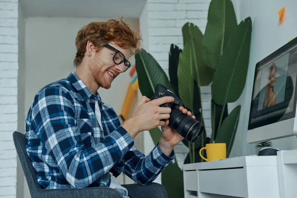 Jovem Feliz Examinando Nova Câmera Enquanto Sentado Seu Local Trabalho — Fotografia de Stock