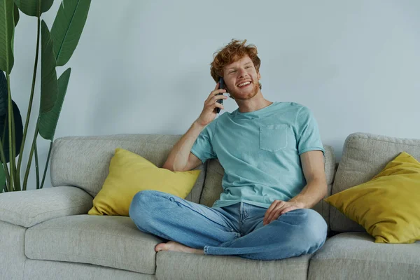 Homem Ruivo Feliz Falando Telefone Celular Enquanto Relaxa Sofá Casa — Fotografia de Stock