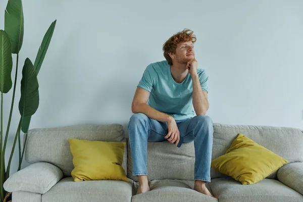 有思想的红头发男人 一边拿着智能手机 一边在家里的沙发上休息 — 图库照片