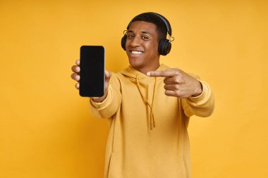 Neşeli, kulaklıklı, akıllı telefonunu gösteren, sarıya karşı duran melez bir ırk.