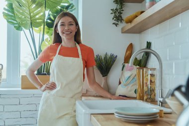 Güzel genç bayan mutfak lavabosunun yanında duruyor ve gülümsüyor.