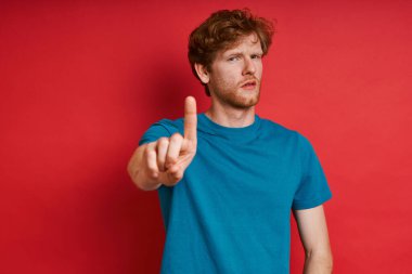 Yakışıklı kızıl saçlı adam kırmızı arka planda dikilirken mola veriyor.