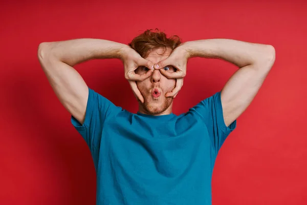 Playful Redhead Man Gesturing Eyeglasses Face While Standing Red Background — Stock Photo, Image