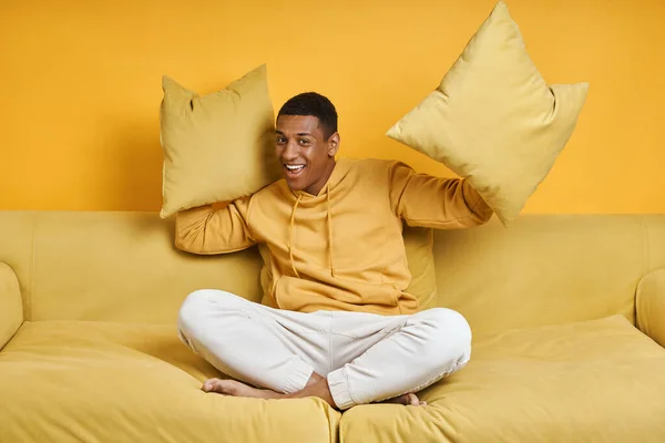 幸せな混合レースマン保持枕ながらソファに座って黄色の背景 — ストック写真
