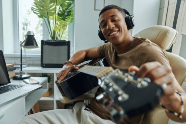 Kendine güveni tam genç bir melez. Akustik gitarını akort ediyor. İş yerinde oturuyor.