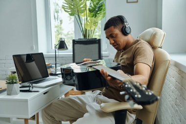 Çalışırken akustik gitarı inceleyen yakışıklı, melez bir genç.