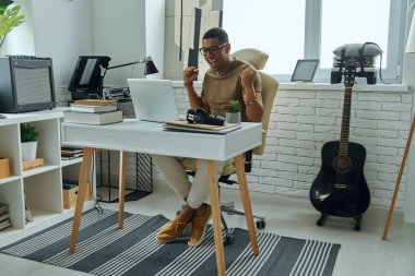 Heyecanlı genç melez adam ofiste dizüstü bilgisayara bakarken el kol hareketi yapıyor.