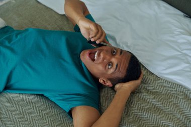 Şaşırmış melez adamın yatakta yatarken cep telefonuyla konuşmasının en üst görüntüsü.