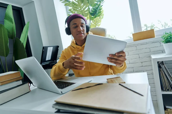 坐在工作位置时 坐在耳机里自信的混血男子使用技术 — 图库照片