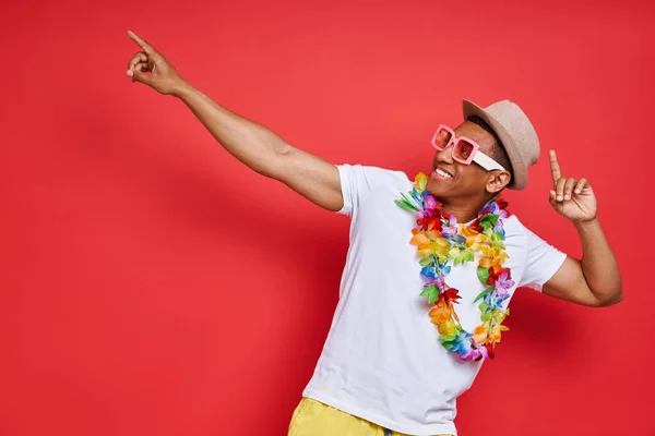 Gelukkige Jongeman Hawaïaanse Ketting Wijzend Weg Terwijl Staan Tegen Rode — Stockfoto