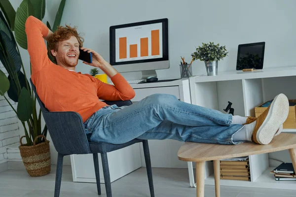 Веселый Молодой Человек Разговаривает Мобильному Телефону Сидя Своем Домашнем Офисе — стоковое фото