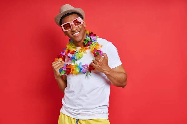 Przystojny Młody Mężczyzna Hawajskim Naszyjniku Wygląda Szczęśliwego Stojąc Czerwonym Tle — Zdjęcie stockowe