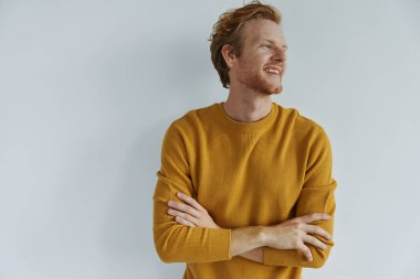 Neşeli genç kızıl saçlı adam kollarını duvara dayayıp çapraz yapıyor.