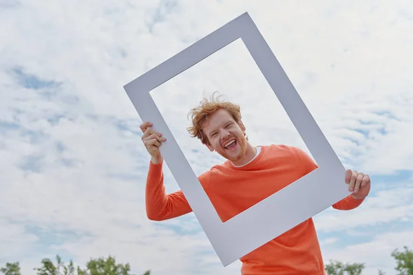 Happy Young Redhead Man Looking Picture Frame Smiling While Standing — Stock Photo, Image