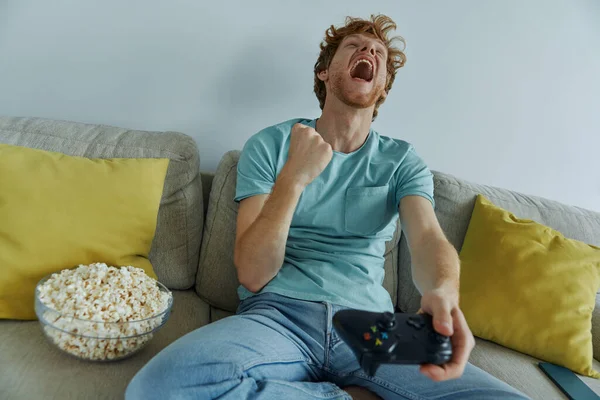 Šťastný Mladý Muž Hraje Videohry Gestikulace Zatímco Sedí Gauči Doma — Stock fotografie