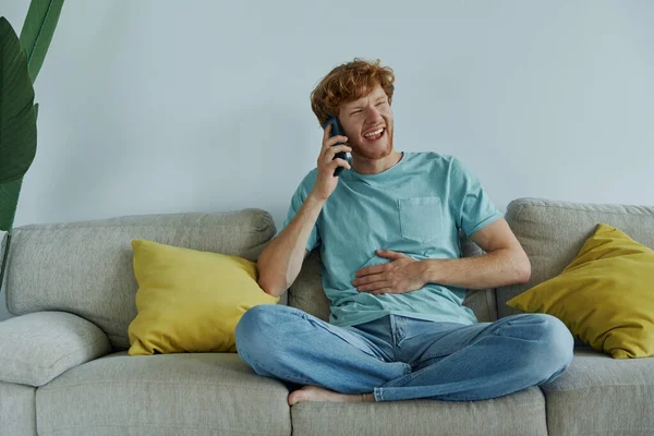 快乐的红头发男人一边在家里的沙发上一边用手机聊天 — 图库照片