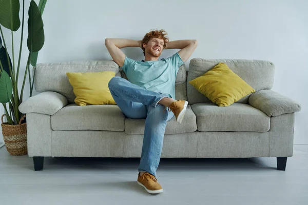 Cheerful Redhead Man Holding Hands Head While Relaxing Couch Home — Stockfoto