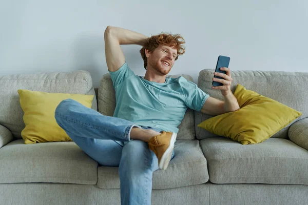 Bello Uomo Rossa Utilizzando Smart Phone Mentre Rilassa Sul Divano — Foto Stock