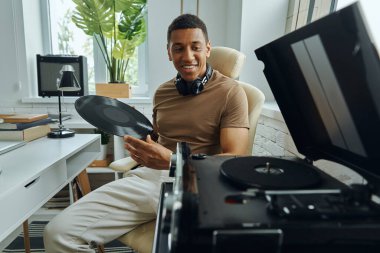 Pikabın yanında oturan kendine güvenen genç Afrikalı adam plak plağı tutuyor.