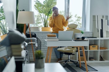 Ofiste çalışırken cep telefonuyla konuşan neşeli, genç bir Afrikalı.