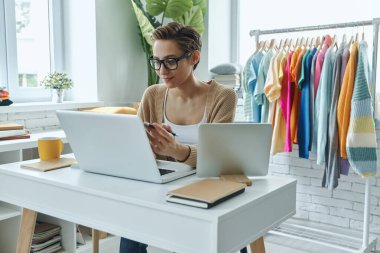 Moda mağazasında çalışırken dizüstü bilgisayar kullanan zarif bir genç kadın.