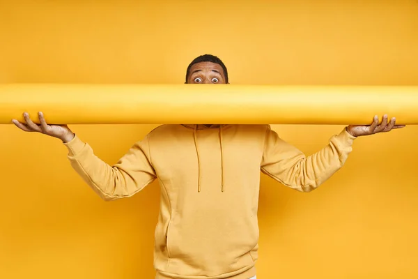 Playful African Man Carrying Rolled Yellow Wallpaper While Standing Yellow — Stockfoto