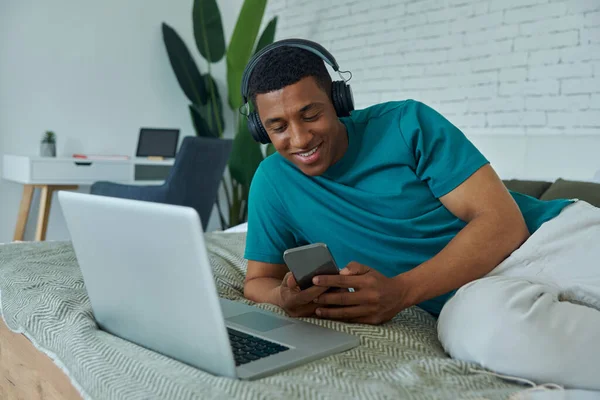 Cheerful African Man Headphones Using Smart Phone While Lying Bed — Stockfoto