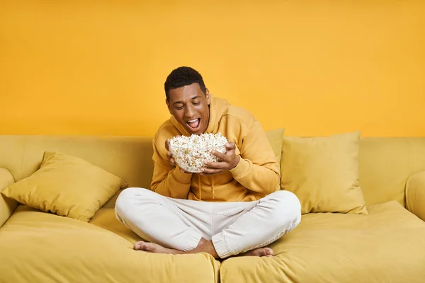 Zabawny Afrykanin Jedzący Popcorn Podczas Relaksu Kanapie Żółtym Tłem — Zdjęcie stockowe