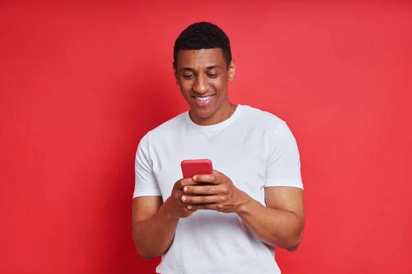 Cheerful African Man Using Smart Phone While Standing Red Background — Stockfoto