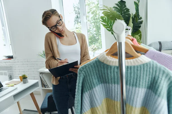 ファッション店で働きながらノートパッドを使う陽気な若い女性 — ストック写真