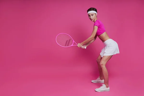 站在粉色背景下拿着网球拍的漂亮年轻女子 — 图库照片