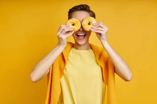 Игривая Женщина Держит Два Пончика Перед Глазами Стоя Жёлтом Фоне — стоковое фото