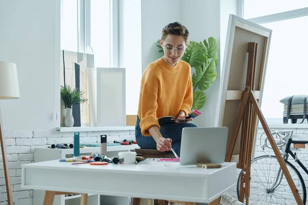 Confident young woman mixing colors while drawing in art studio