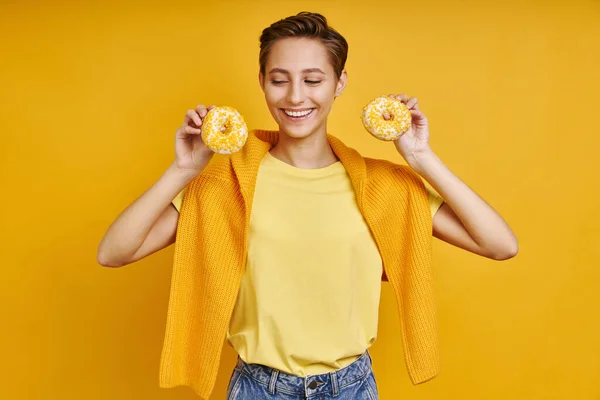 Красивая Молодая Женщина Держит Два Пончика Стоя Желтом Фоне — стоковое фото