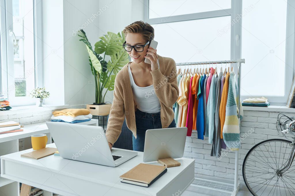 Cheerful young woman talking on mobile phone while working in fashion store office