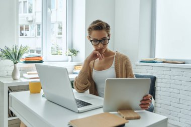 Concentrated young woman using technologies while working in creative office