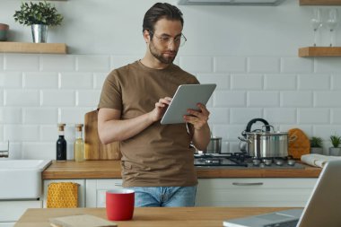 Kendine güveni tam genç bir adam ev mutfağında çalışırken teknolojiyi kullanıyor.