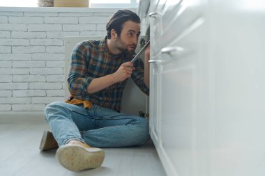 Ev mutfağında lavabo tamir ederken İngiliz anahtarı kullanan kendine güvenen genç adam.