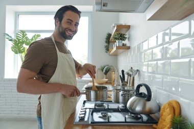 Neşeli genç adam fırında bir şeyler pişirirken evcil mutfakta duruyor.