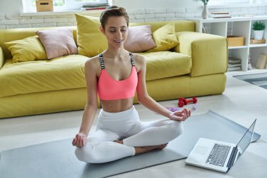 Spor elbiseli güzel bir kadın evde meditasyon yapıyor.