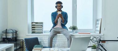 Confident African man using smart phone while sitting on the window sill in office